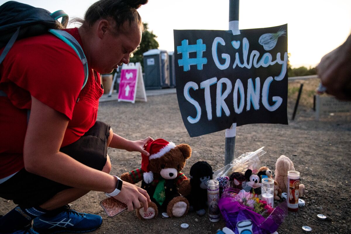 Laura Miller places a stuffed bear at a memorial for those who died in the shooting at the Gilroy Garlic Festival.