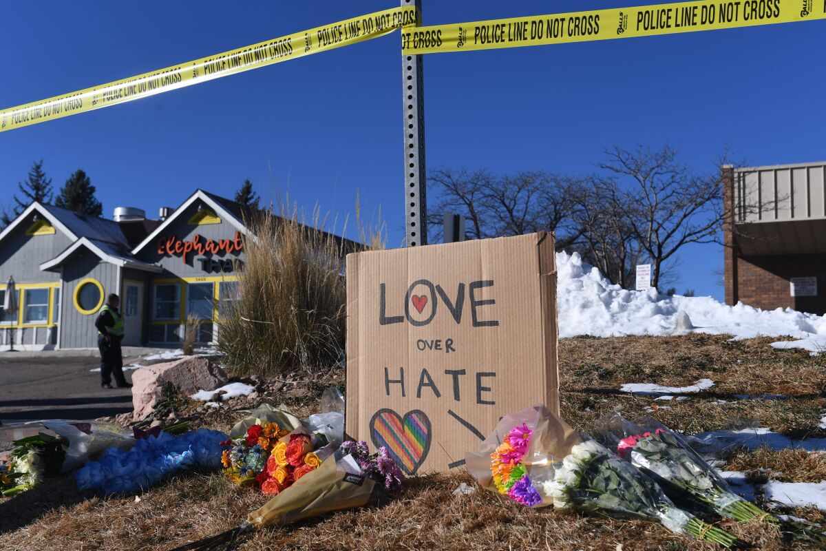 Bouquets and inscription on the sign "Love over hate" on the ground next to police tape.
