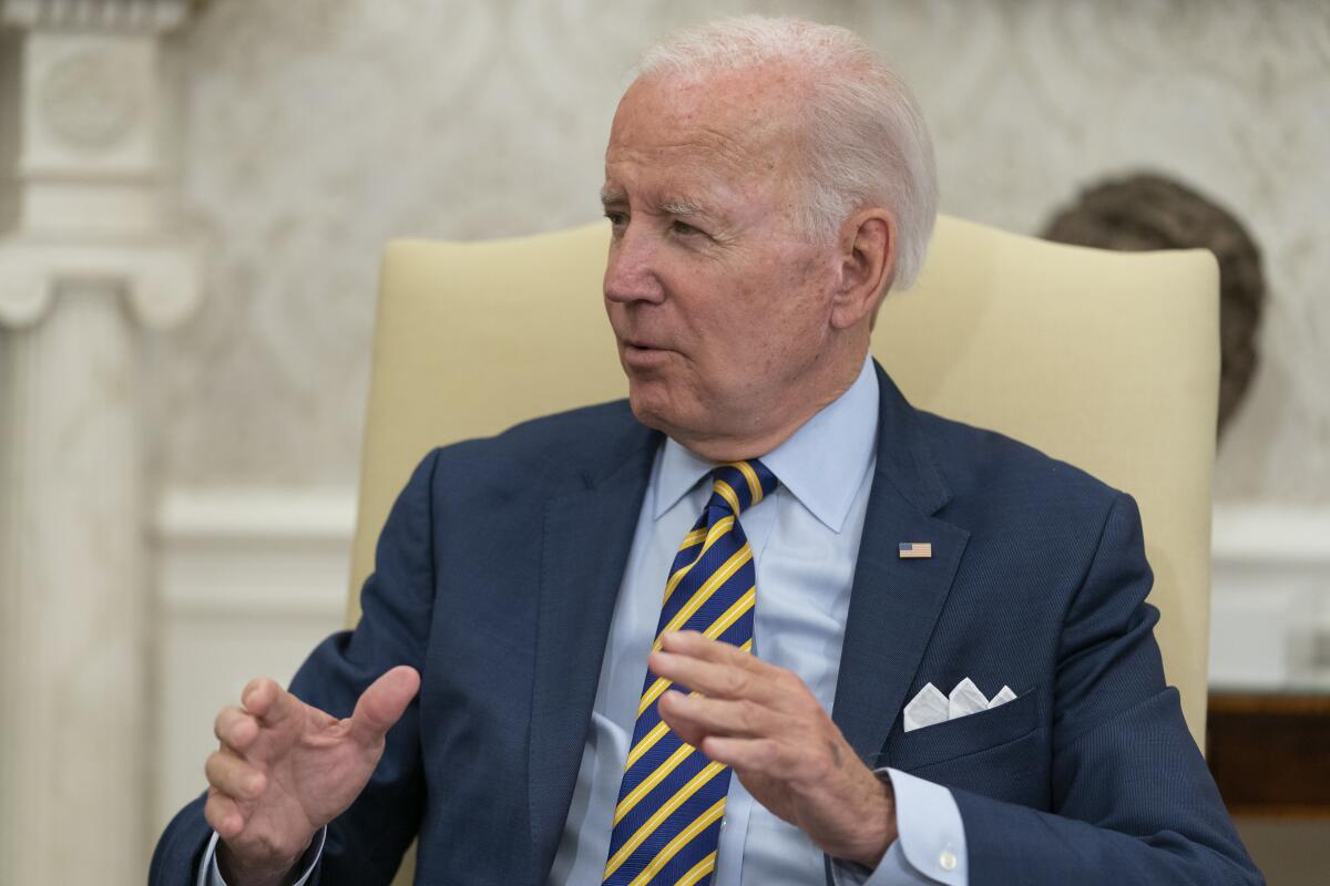 President Biden, seated, gestures while speaking