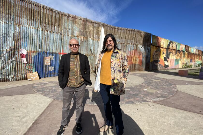 Los integrantes de Nortec, Ramòn Amezcua Bostich (saco negro) y Pepe Mogt Fussible (playera amarilla), frente al muro fronterizo en Playas de Tijuana.