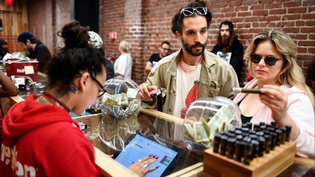 A woman looks at a marijuana strain at MedMen, standing next to a man and across the counter from a woman working on a touchscreen.