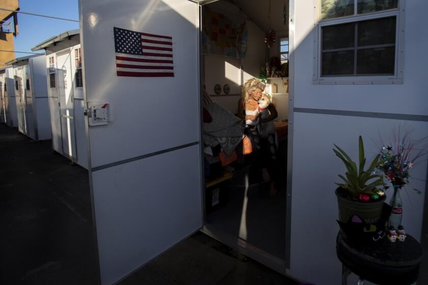 RIVERSIDE, CA - NOVEMBER 30, 2020: Karen Morea, 62, hugs her dog Jack-Jack inside her tiny village home in a parking lot adjacent to a Riverside shelter on November 30, 2020 in Riverside, California. She has been here almost two months after living on the streets. Los Angeles is embracing the idea of tiny homes to get homeless off the streets, but the buildings are sitting in storage.(Gina Ferazzi / Los Angeles Times)