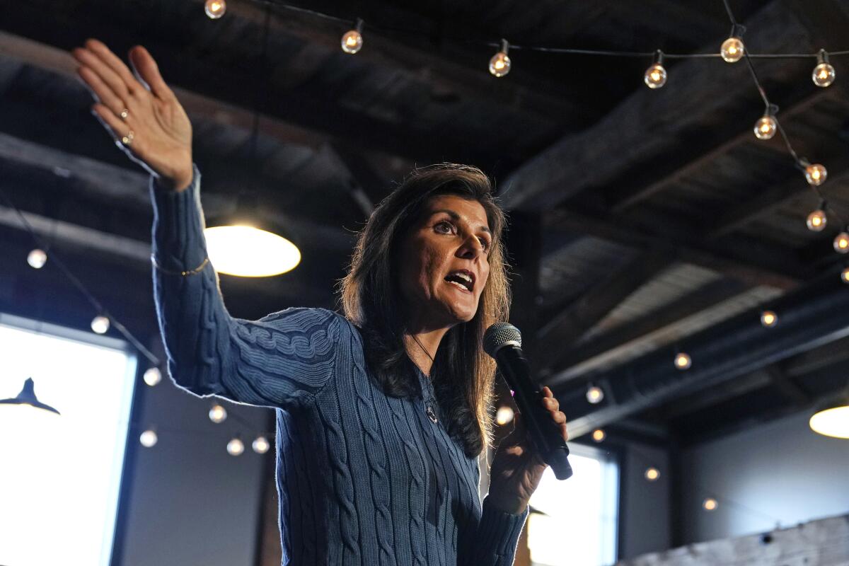 Nikki Haley pictured from the waist up, extending her right arm as she speaks into a large microphone in her left hand