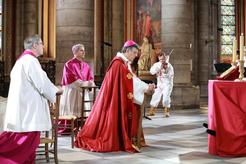 Notre-Dame de Paris cathedral's rector Patrick Chauvet, left, Auxiliary Bishop of Paris Denis Jachiet and Archbishop of Paris Michel Aupetit attend a ceremony to celebrate Good Friday while violinist Renaud Capucon performs, in a secured part of Notre-Dame de Paris cathedral Friday, April 10, 2020, in Paris. Although still damaged and scarred by fire, Notre Dame Cathedral has — if only for an instant — come back to life as a center for prayer in a Paris locked down against the coronavirus. The new coronavirus causes mild or moderate symptoms for most people, but for some, especially older adults and people with existing health problems, it can cause more severe illness or death.(Ludovic Marin, Pool via AP)