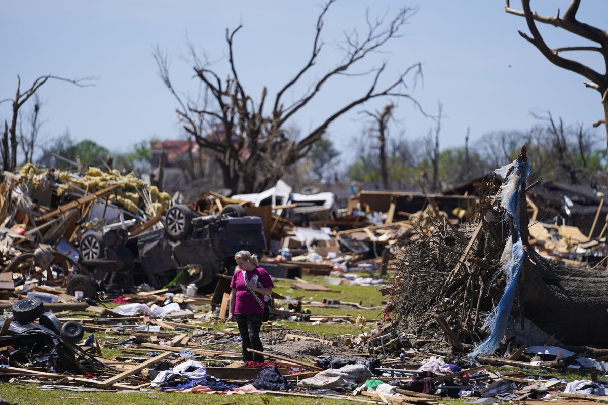 A woman walks near an uprooted tree, a flipped vehicle and debris from homes damaged by a tornado, Monday, March 27, 2023, in Rolling Fork, Miss. (AP Photo/Julio Cortez)