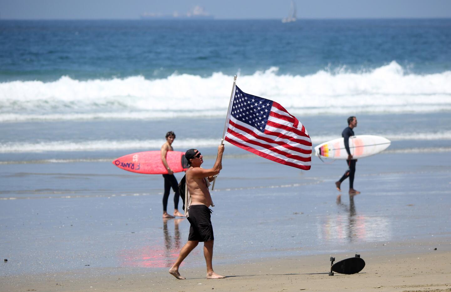 A man flies the USA flag before the protest at Main Street and Pacific Coast Highway in Huntington Beach on Friday.