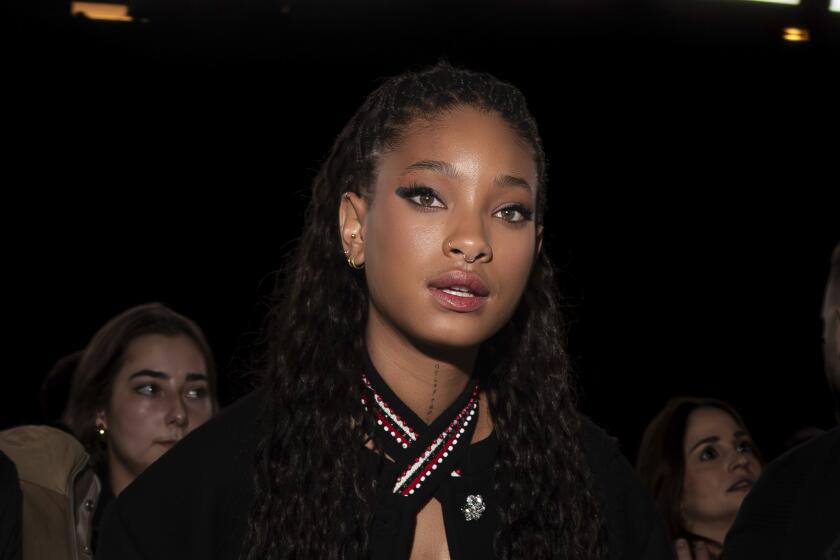 Willow Smith in a dark top posing with her mouth slightly open in a dark room