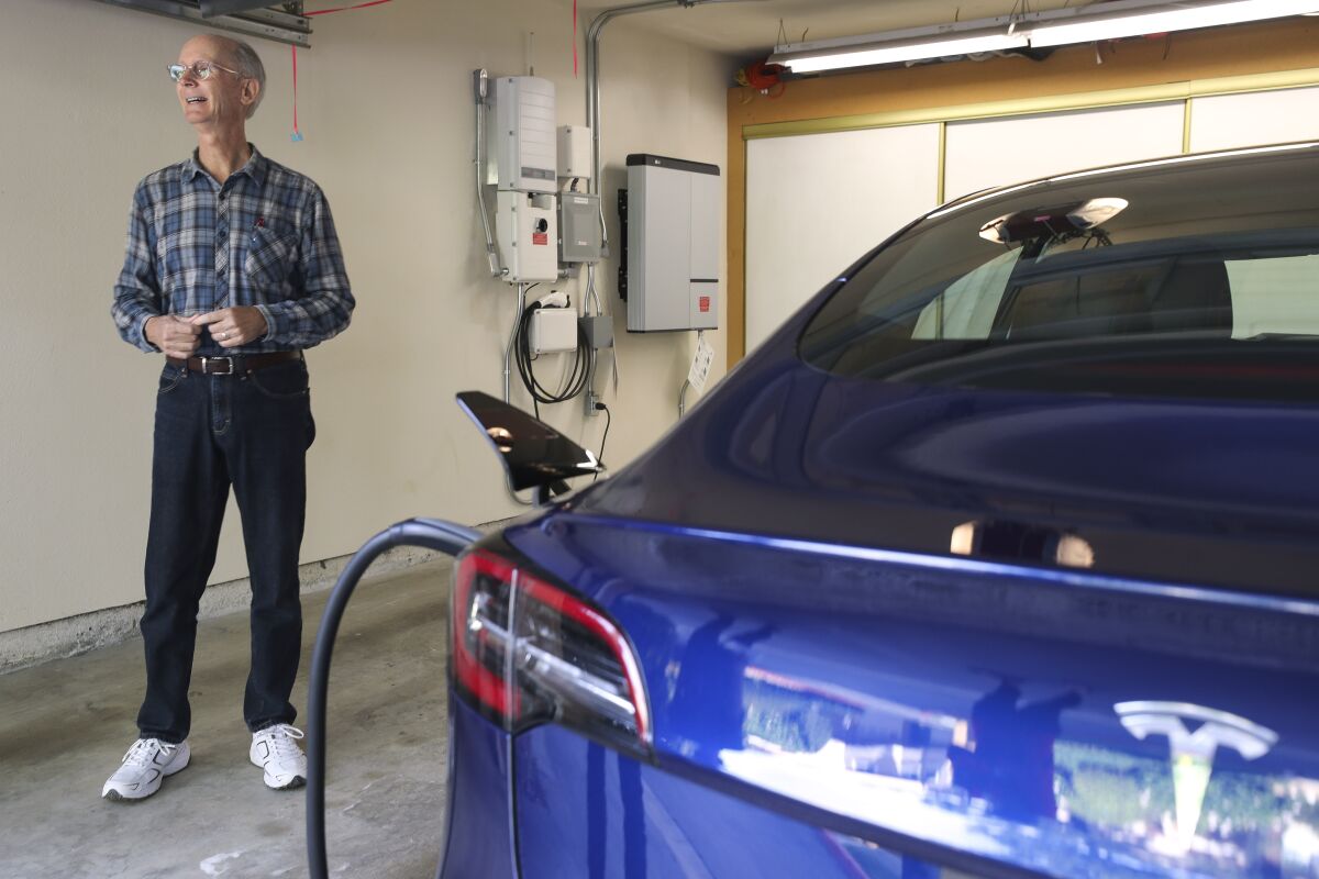 Mark Hughes stands in between his Tesla Model 3 electric car and his LG Chem residential energy storage unit, background, while in the garage of his condominium on Tuesday.