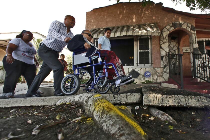 Bernard Parks Jr., chief of staff of Councilman Bernard Parks, pushes Helen Young, 80, in a wheelchair over a broken sidewalk in front her home on West Century Boulevard in Los Angeles, where Councilman Parks and the L.A. Neighborhood Initiative marked the start of several sidewalk repair projects.