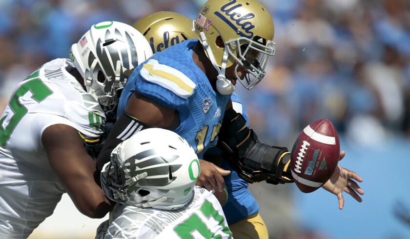 UCLA quarterback Brett Hundley fumbles as he is hit by Oregon linebacker Tony Washington (91) and defensive lineman T.J. Daniel (45) in the first quarter Saturday at the Rose Bowl.