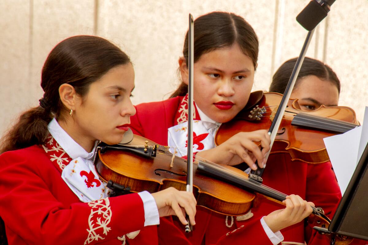 Two girls in red mariachi outfits playing violins 