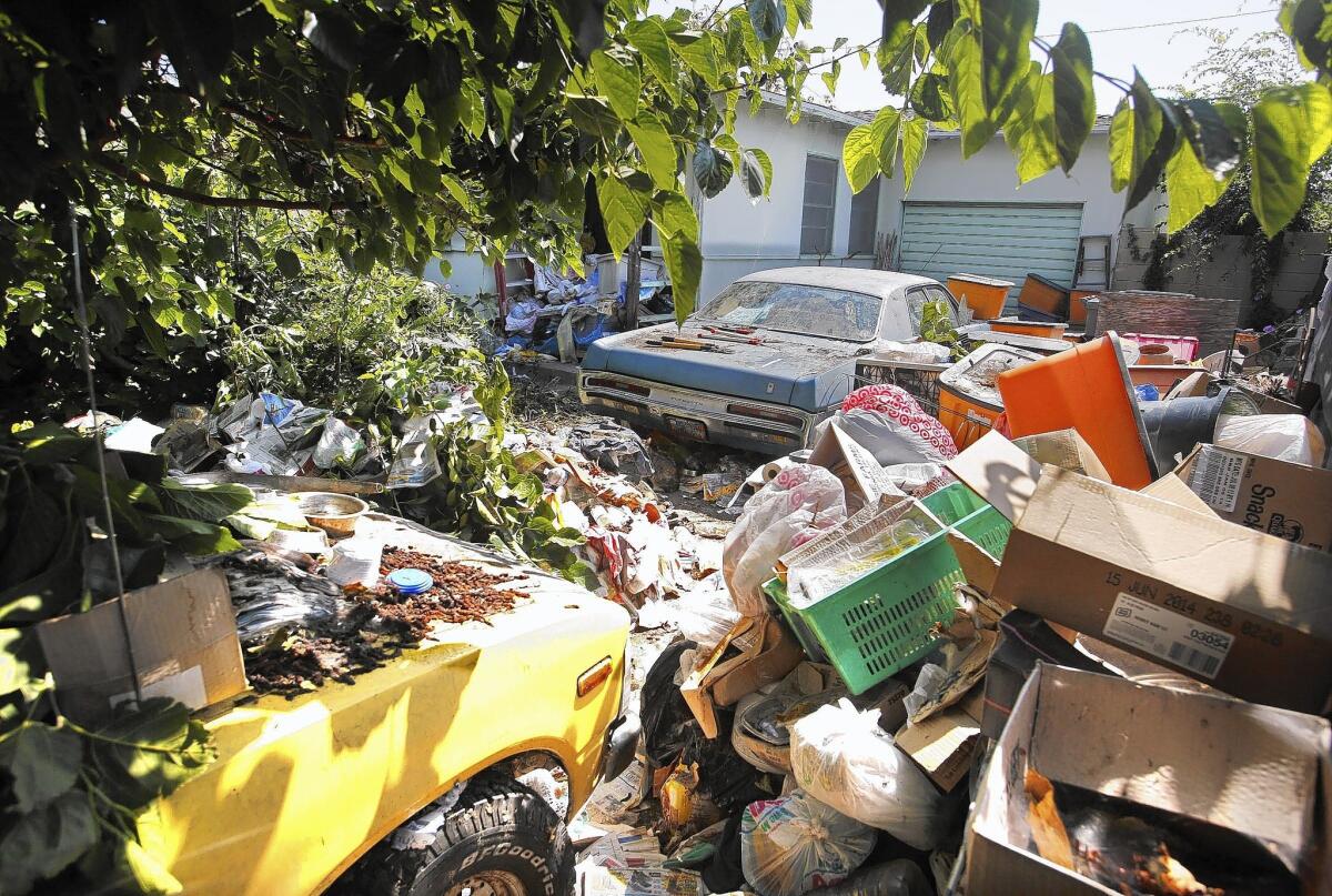 Trash and vehicles fill the front yard of a house on Rosewood Street in Santa Ana. Emergency crews worked three hours to remove the dead woman's body.