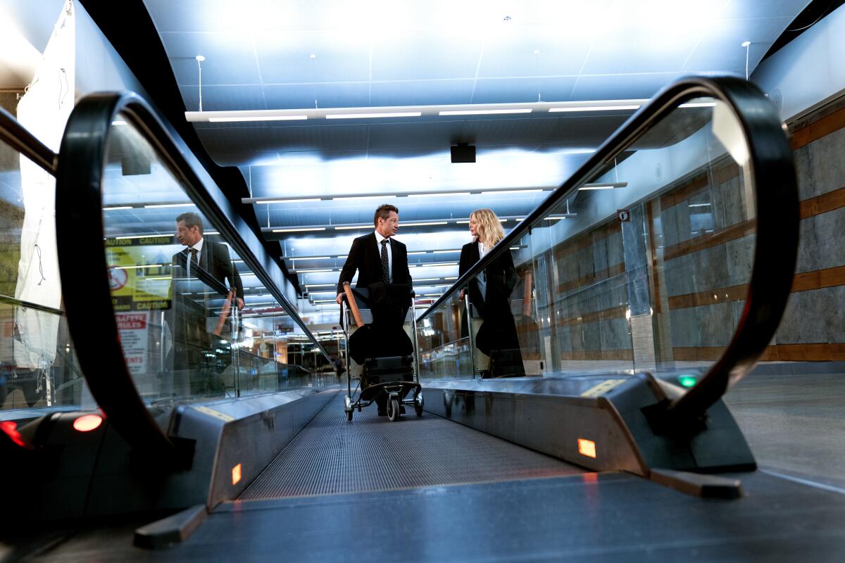 Two people converse on the moving platforms in an airport.