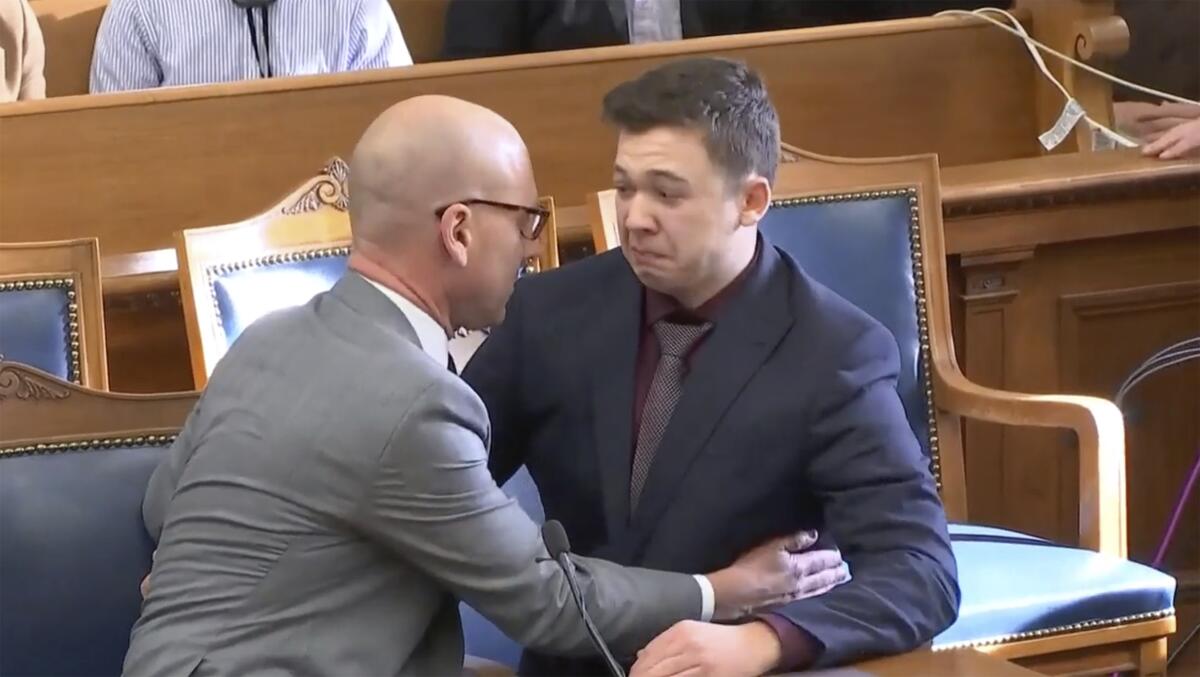 A man in a gray suit comforts a younger man in a courthouse