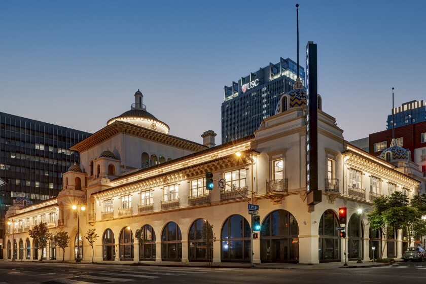 The Herald Examiner building is seen at an angle at dusk, it's windows illuminated from within