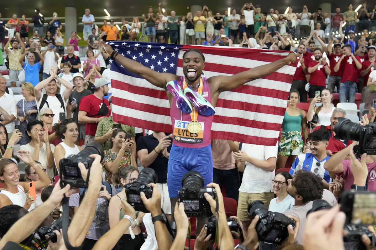 Noah Lyles is draped with an American flag as he celebrates after winning the gold medal in the 200 meters.