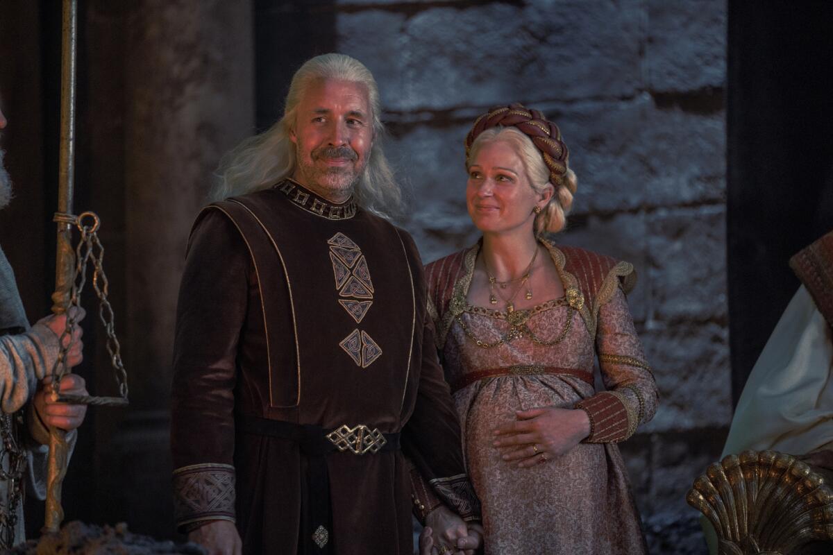 A man and a pregnant woman stand side by side in medieval-looking costumes.
