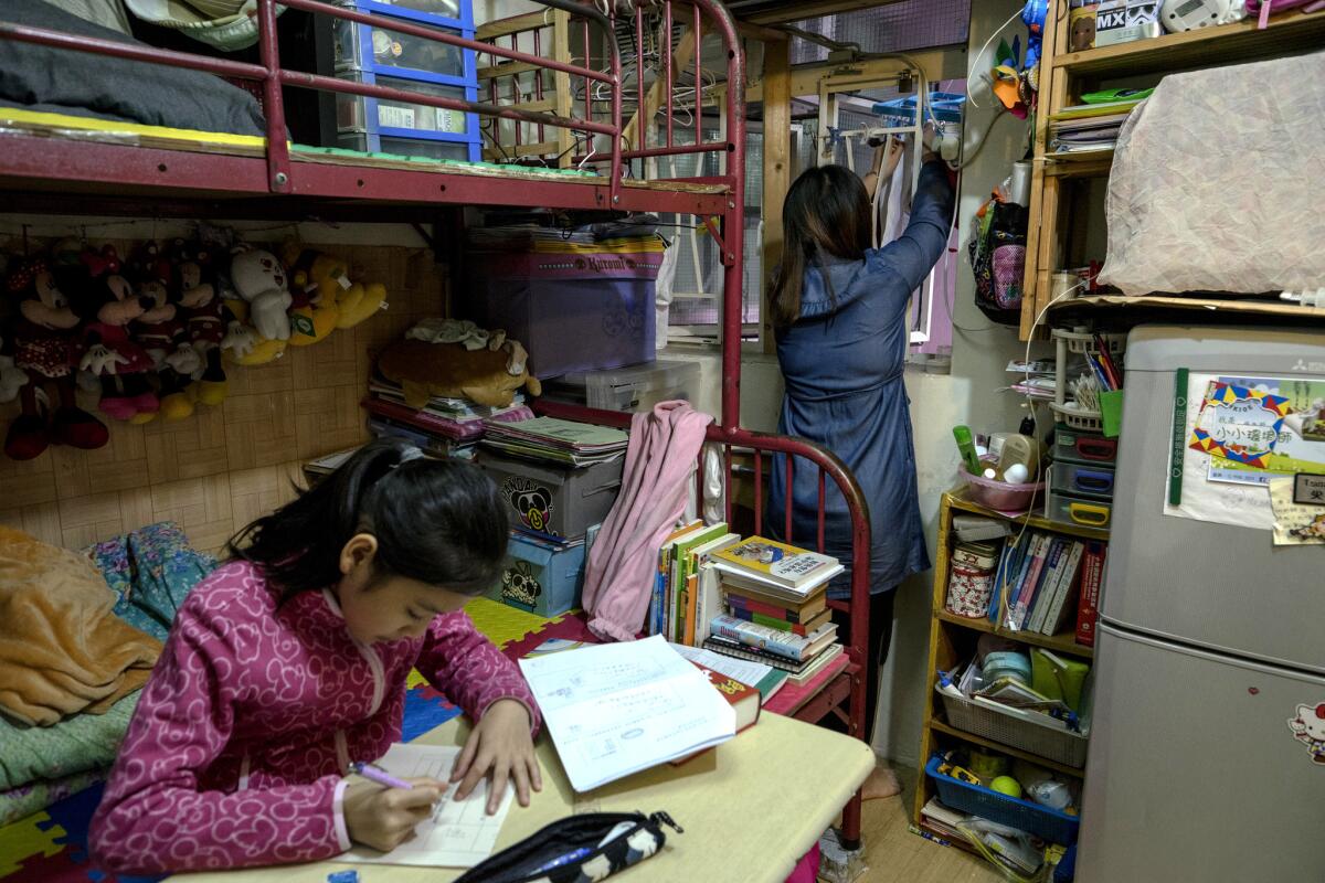 Mai Han does household chores as her daughter, Alice, studies in their one-room flat in Kowloon, Hong Kong.