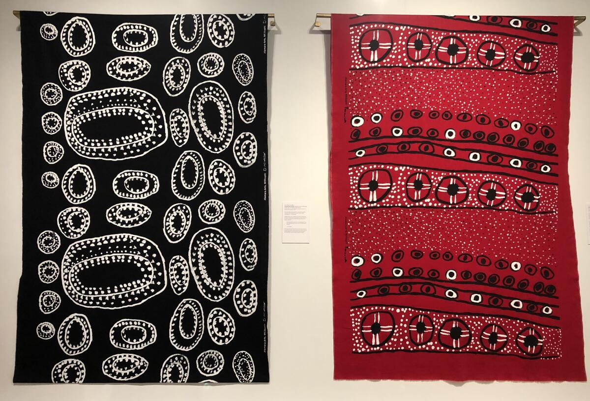 An installation view shows black and red textiles bearing circular patterns. 