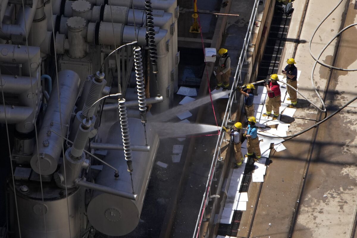 Firefighters spray water after a fire on the Arizona side of the Hoover Dam, Tuesday, July 19, 2022, near Boulder City, Nev. Officials say no one was injured when a transformer at Hoover Dam briefly caught fire Tuesday morning. (AP Photo/John Locher)