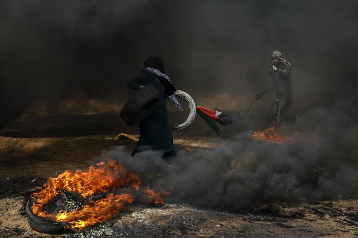 Under the shroud of smoke, Palestinians put more tires into place to burn as they protest at the border fence.