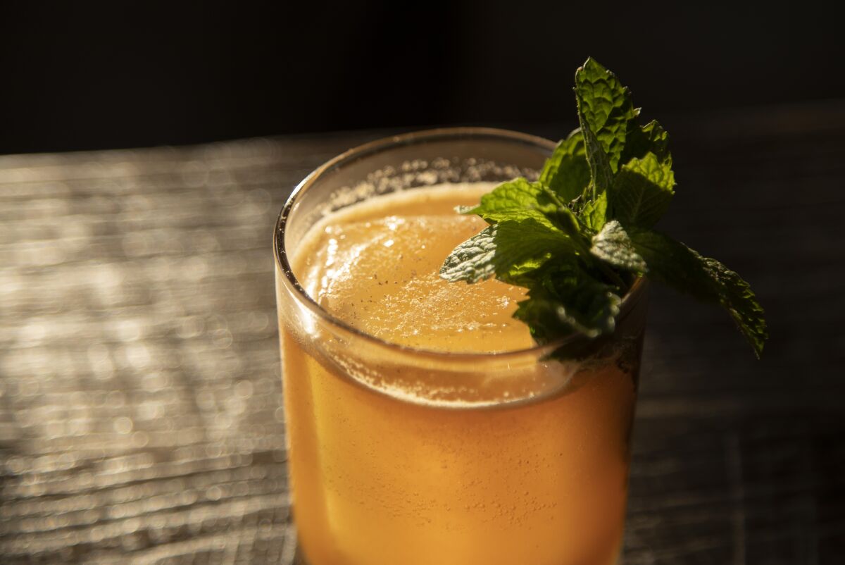 An orange-colored cocktail topped with fresh mint.