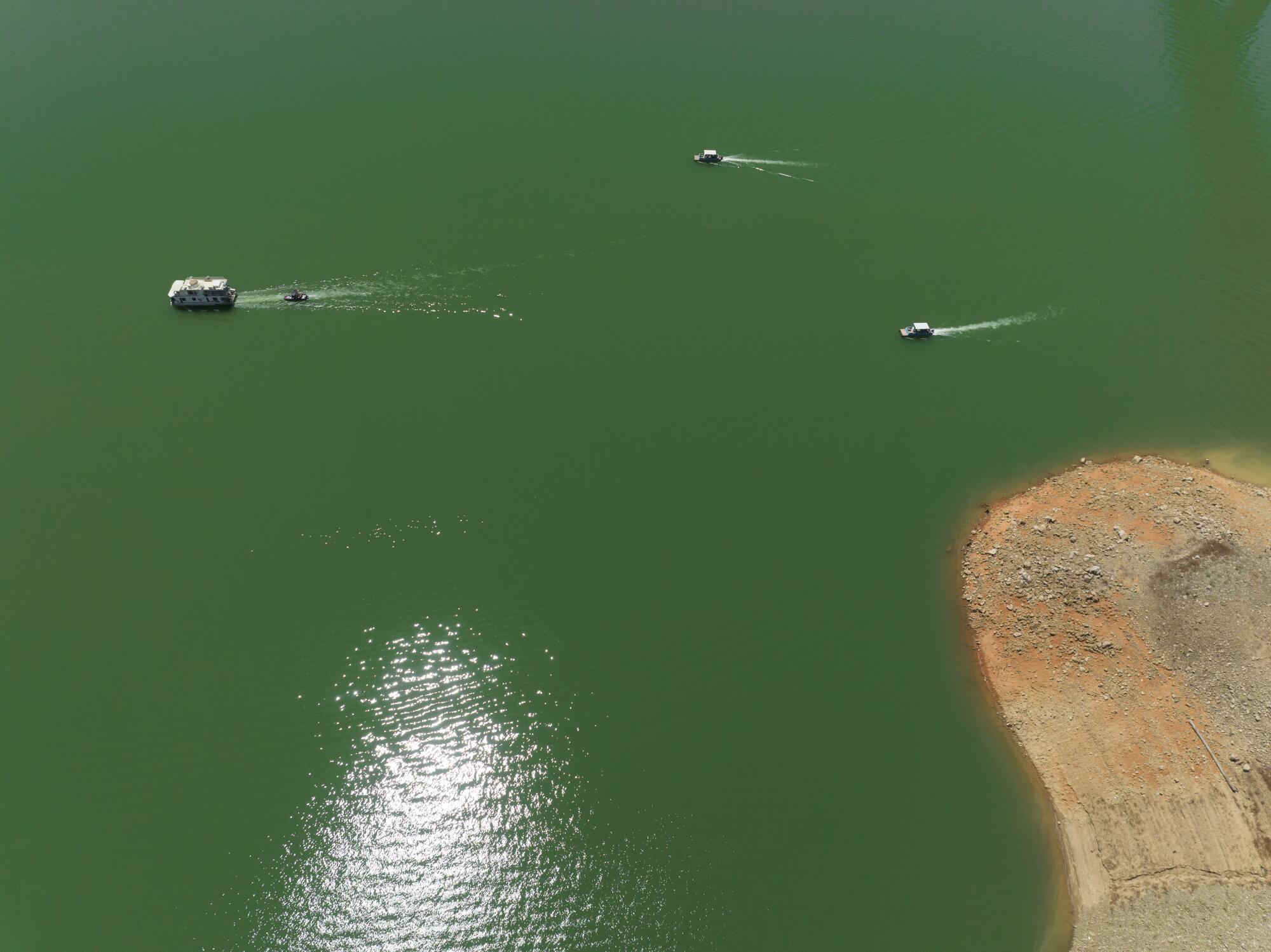 Boats glide through the water at Shasta Lake near exposed shoreline