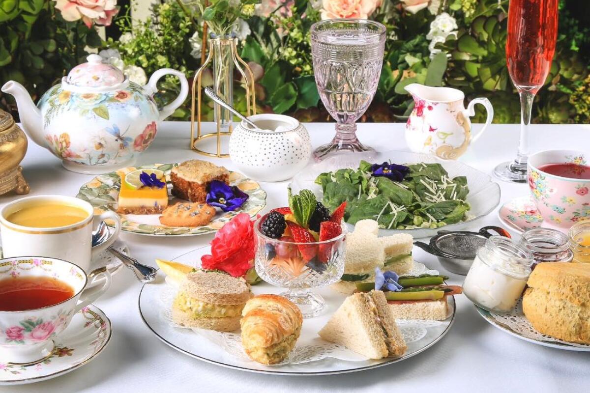 A spread with tea sandwiches, pastries, salad, teacups, a teapot, a glass of water and champagne.