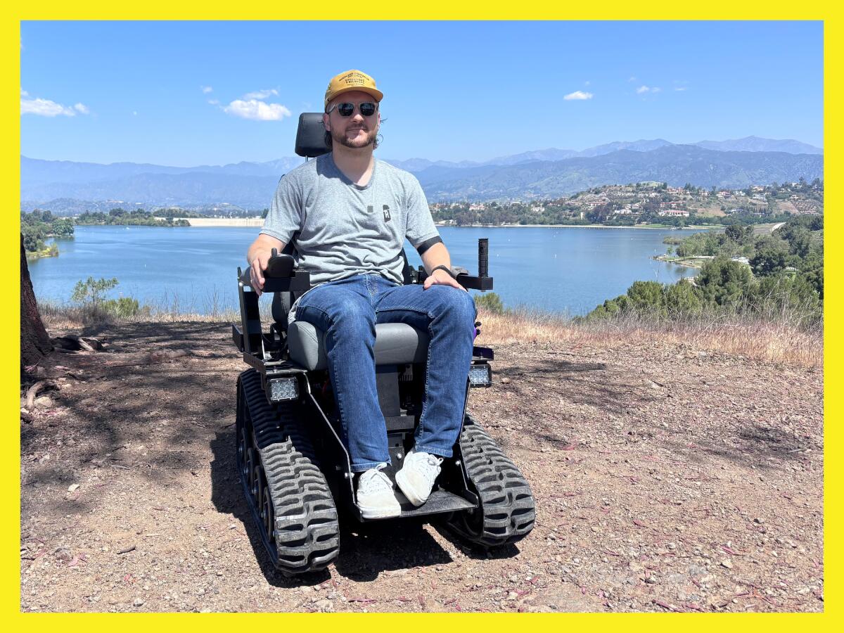 a man sitting in an electric wheelchair on a hiking trail beside a lake