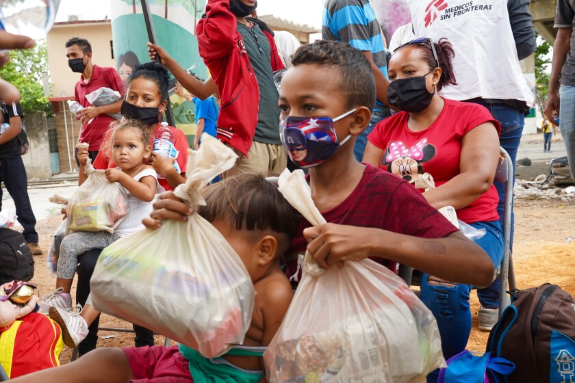 Families sit or walk around, some holding plastic bags of donated goods