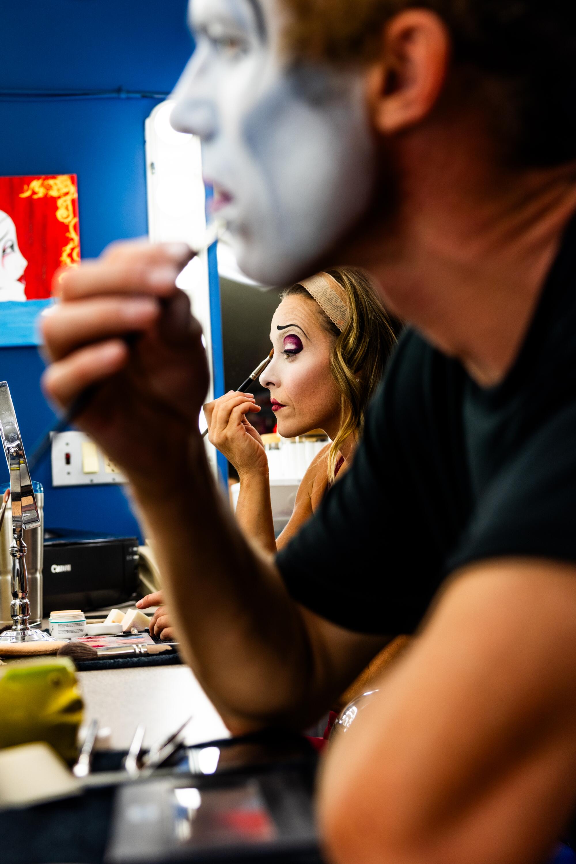Two Cirque du Soleil performers apply makeup backstage.