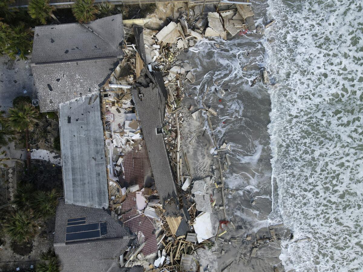 Las olas golpean sobre la playa erosionada bajo una residencia parcialmente colapsada 