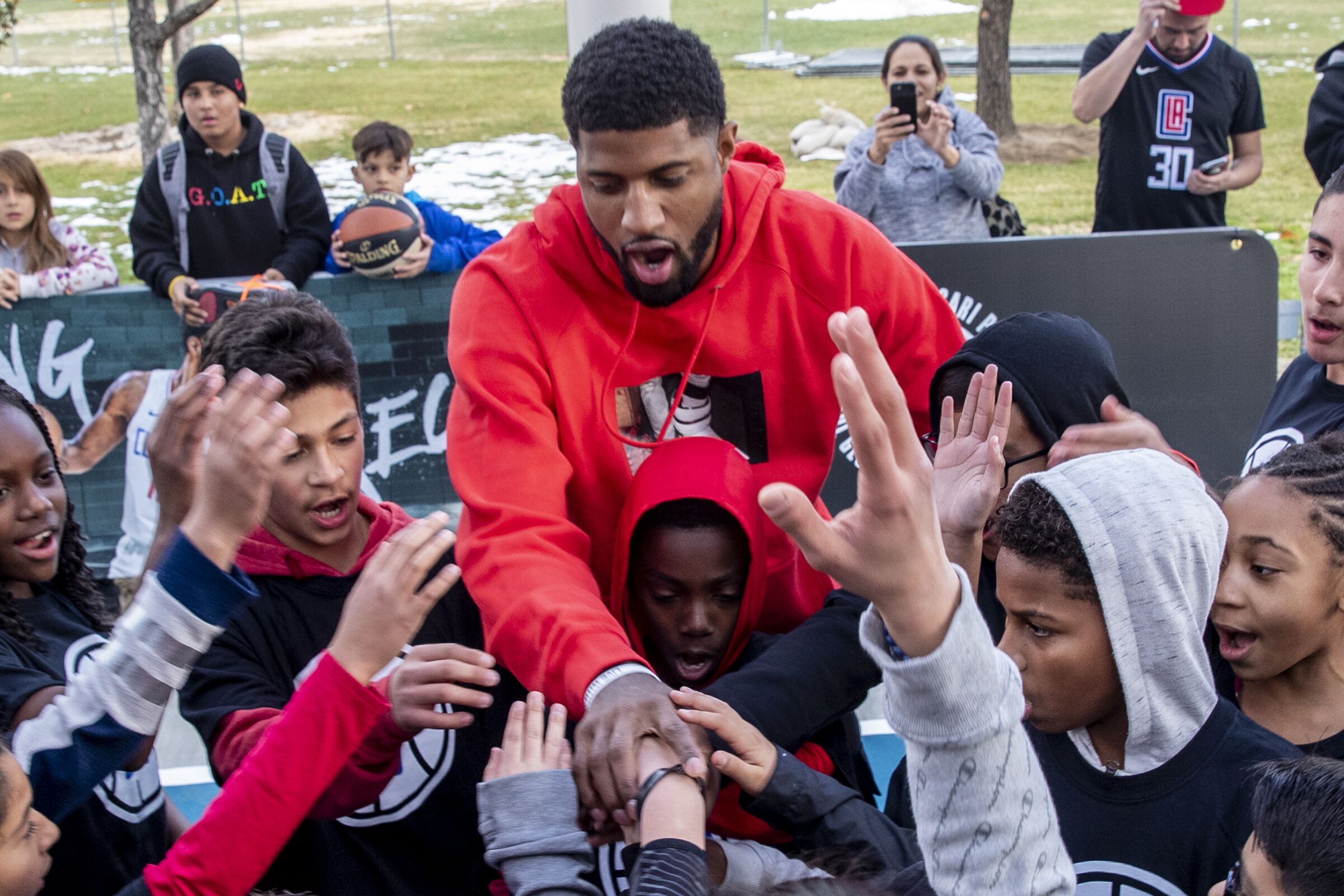 Clippers forward Paul George greets young fans on a basketball court at a park.