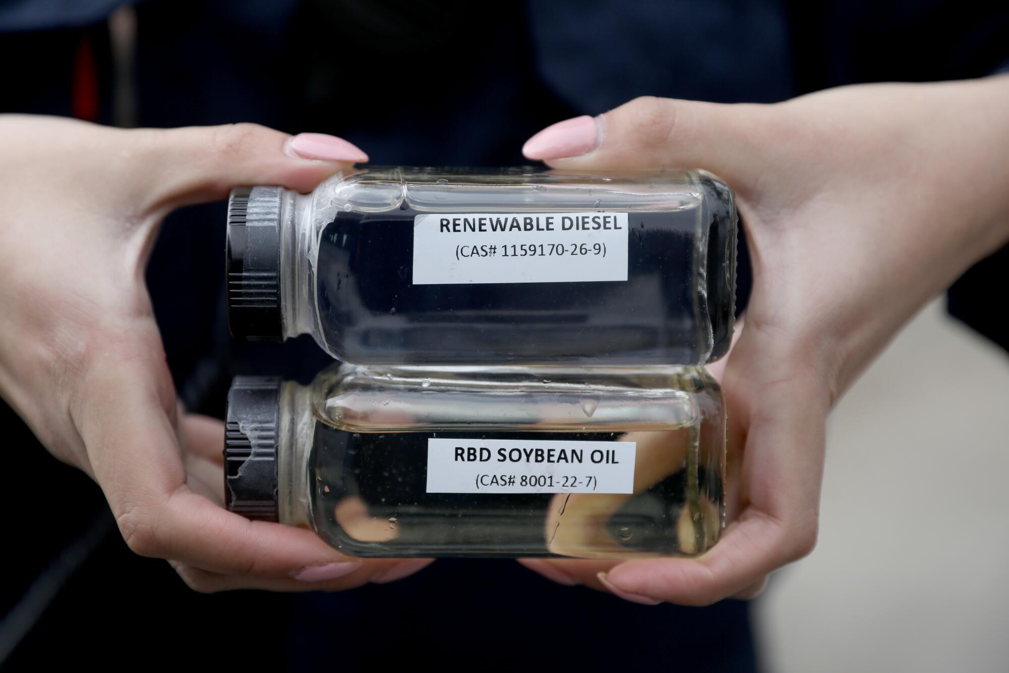 A woman holds two liquid-filled jars with labels identifying them 