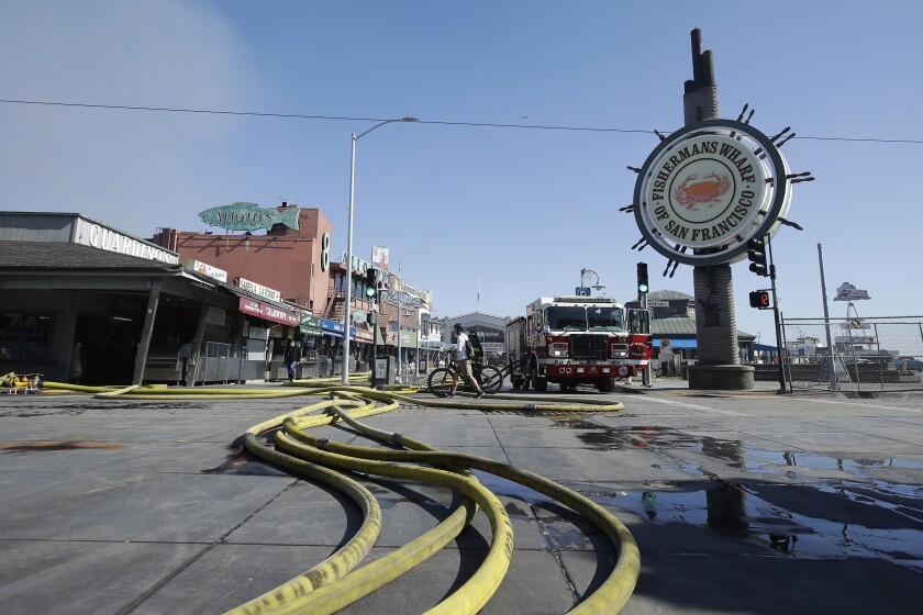 A runner passes over hoses after a fire broke out before dawn at Fisherman's Wharf in San Francisco, Saturday, May 23, 2020.