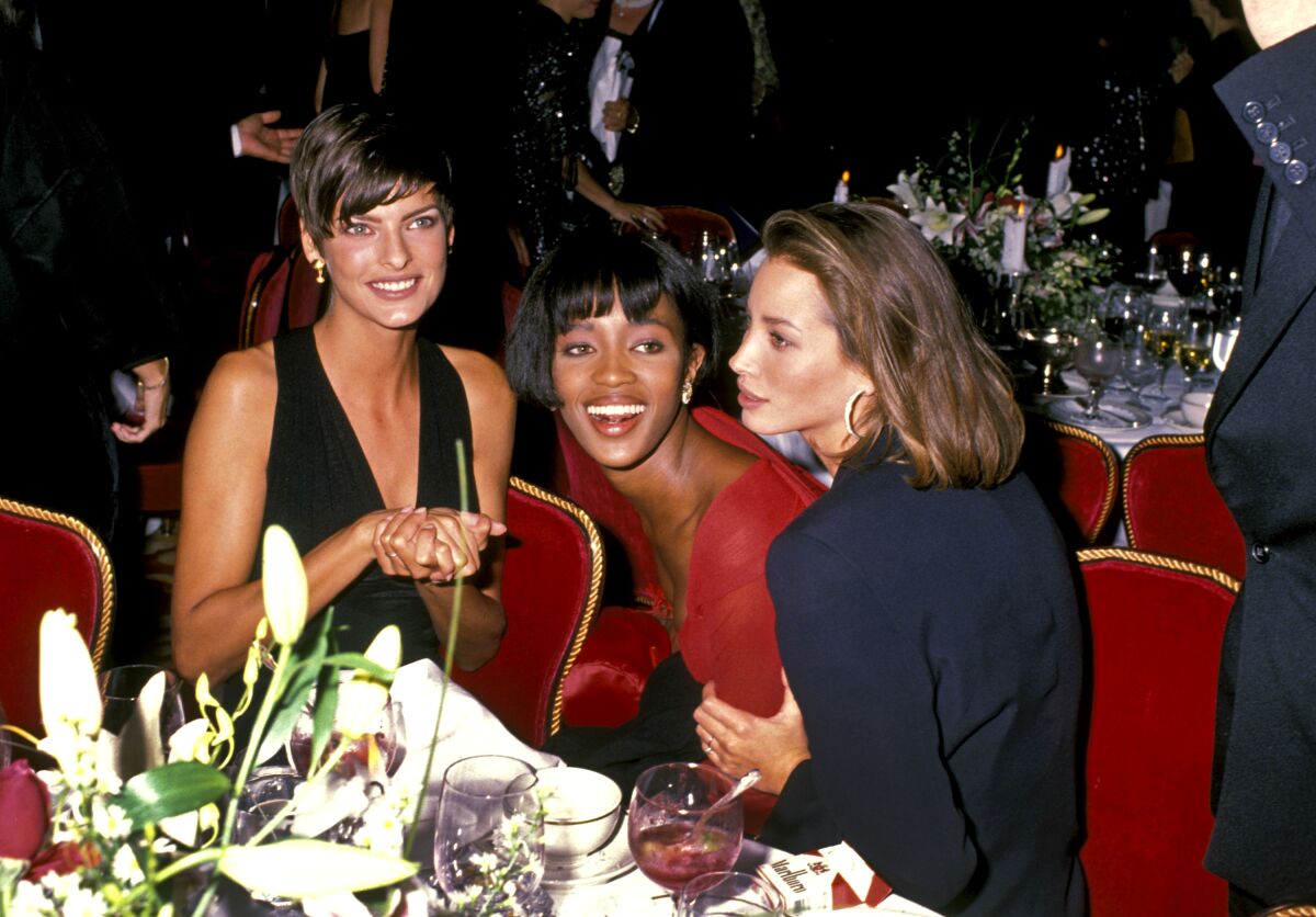 Three women laugh together while seated at an event.