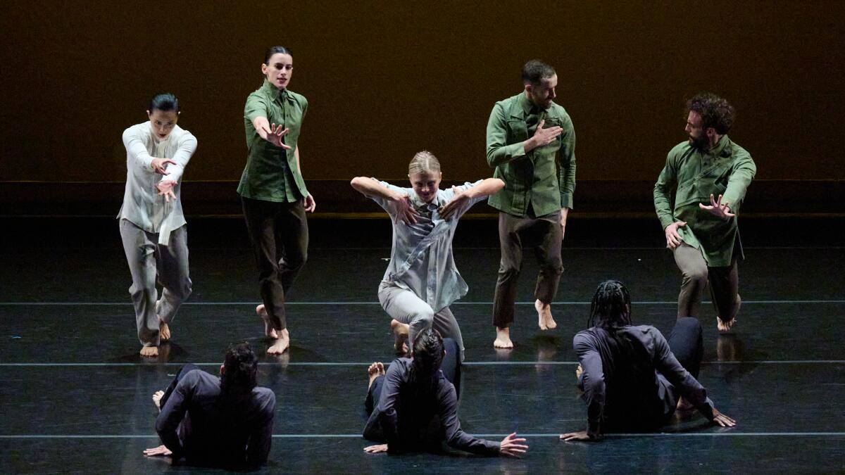 Five dancers standing in front of three dancers in front of them, looking down at them.