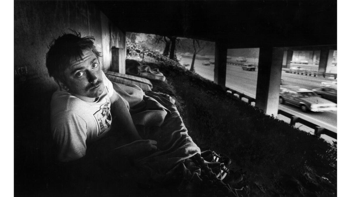 Nov. 8, 1982: Ton Kammer peers up from his bed, a mattress on dirt, beneath an overpass on the Hollywood Freeway. Behind Kammer are other mattresses with one sleeping neighbor.
