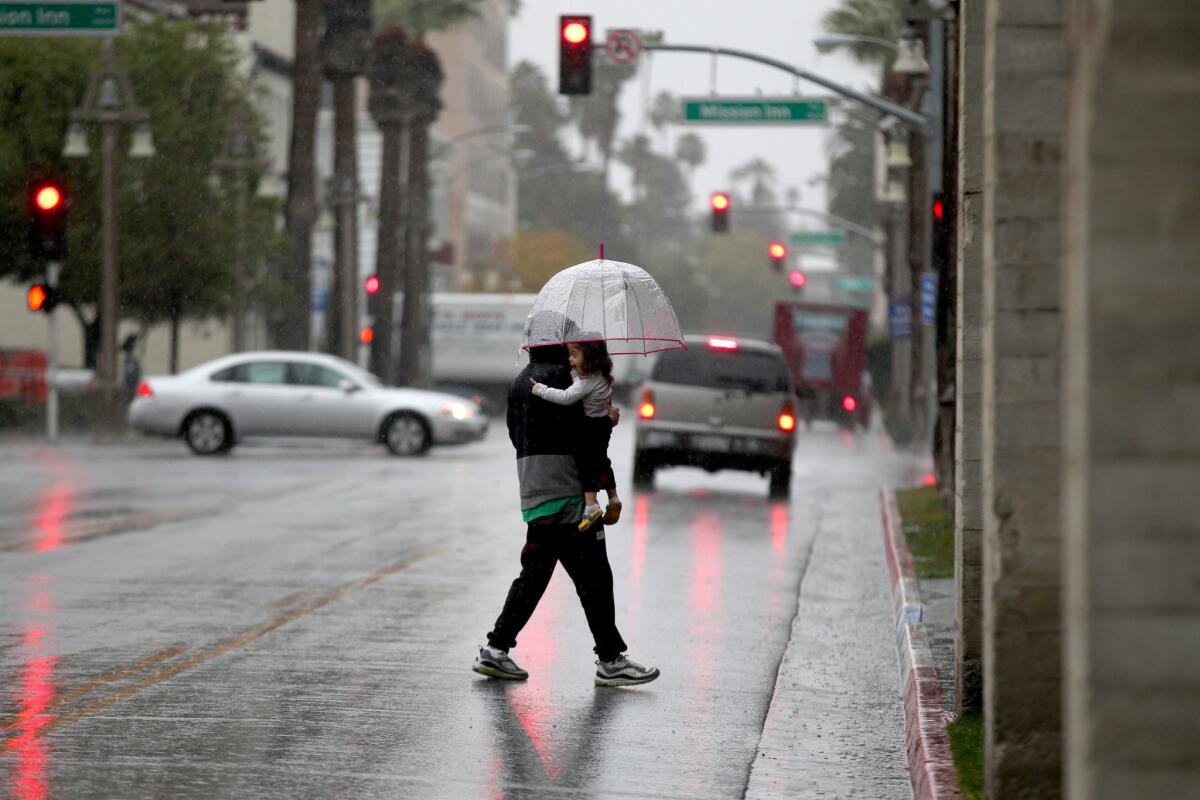 A pedestrian totes a child and an umbrella walking in an El Niño storm in downtown Riverside.