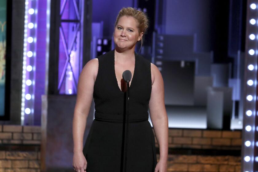A woman in a sleeveless black dress makes a funny face while standing onstage