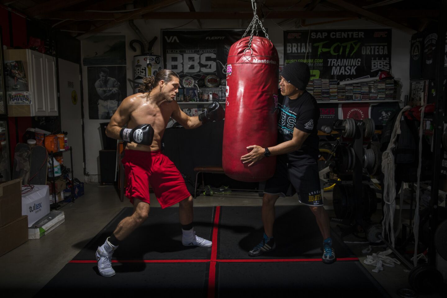 Brian "T-City" Ortega, a UFC featherweight fighter, trains on the heavy bag, in the garage of his coach, James Luhrsen, right, in the Harbor City neighborhood of Los Angeles on Feb. 22, 2018. The two met about 10 years ago in a south bay surf spot and have trained together since.