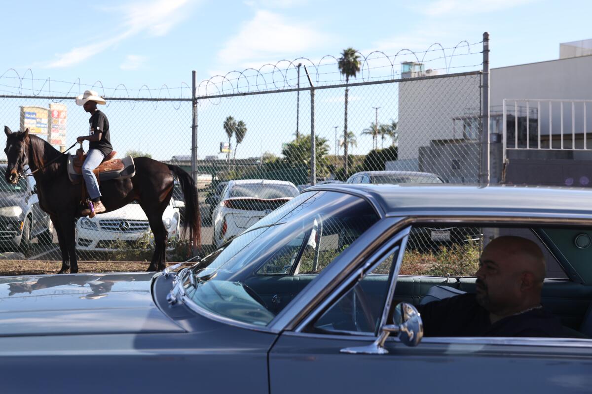 Sam Jones, left, rides his horse, as low riders drive pass during a ceremony honoring Eazy-E.