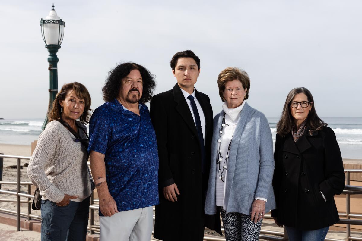 Three women and two men stand on a sidewalk in front of a ramp to a beach.