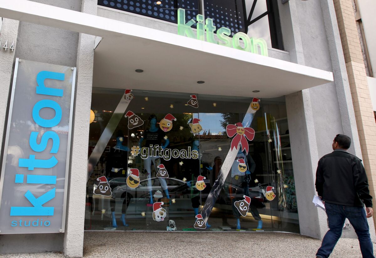 A man walks past a storefront with holiday decorations and the word "kitson" above the entrance and on one side