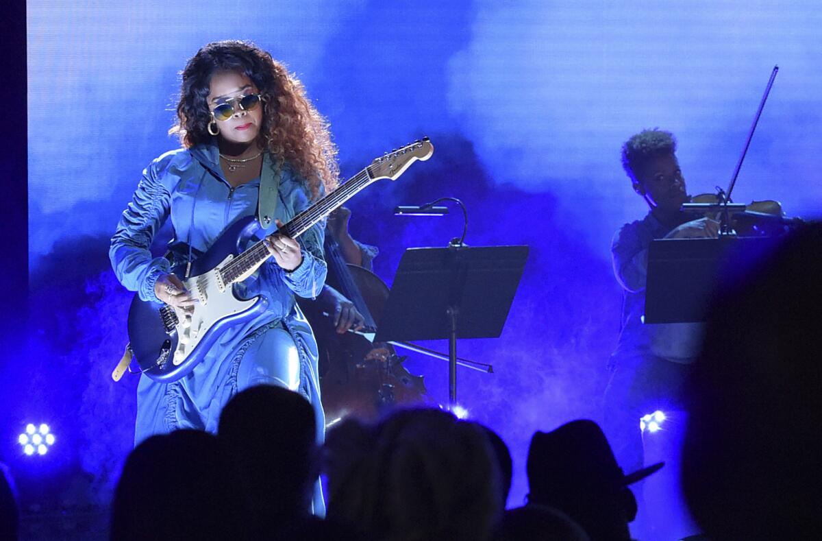 H.E.R., in sunglasses, plays the guitar onstage.
