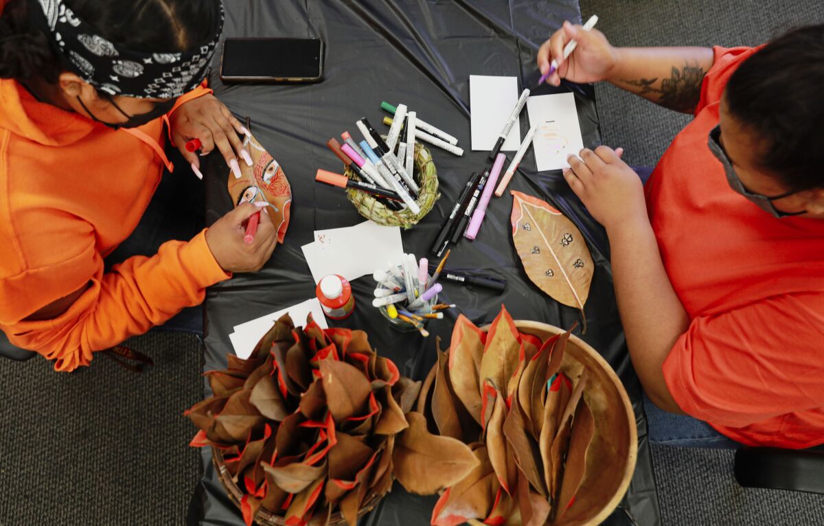two people wearing orange shirts draw on leaves while sitting at a table