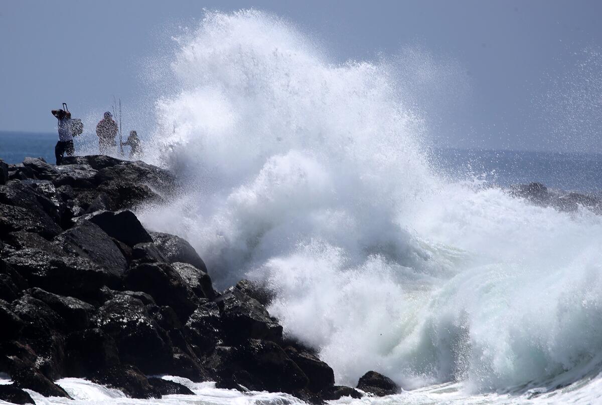 Fishermen are dwarfed by a big wave crashing at The Wedge in Newport Beach on July 20.