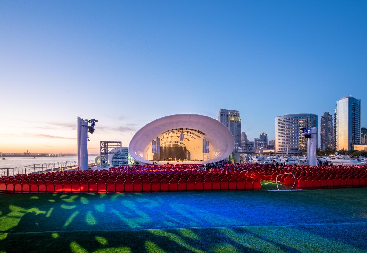 A view of the Rady Shell at dusk shows golden light falling on the shell and on the San Diego skyline in the distance