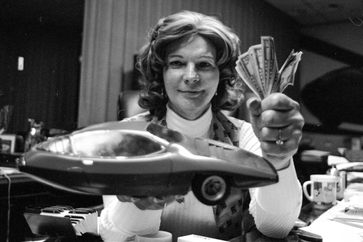 A black-and-white photo of a woman holding a model car and a handful of cash