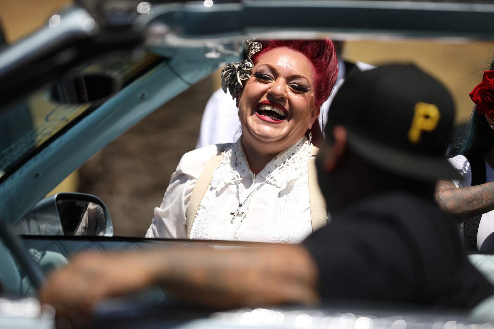 A woman, standing outside a car, laughs as she talks with the driver.